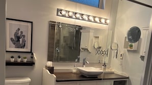 Ein modernes Badezimmer mit Duschkabine aus Glas, einem Waschtisch mit großem Spiegel und einem gerahmten Kunstwerk über dem Waschbecken.