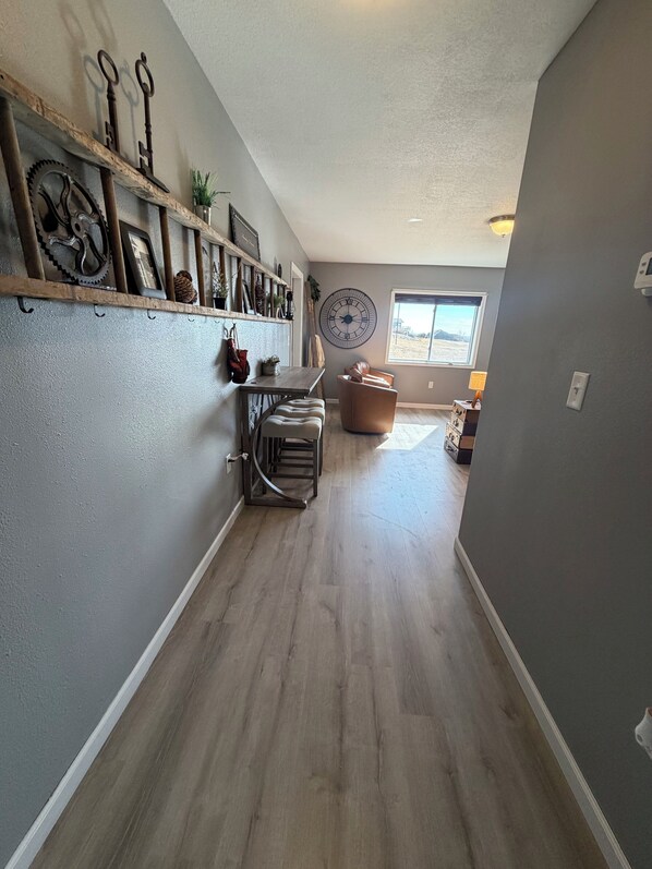 A spacious hallway with a wooden floor, a large wall clock, and a window with a view of the outdoors.