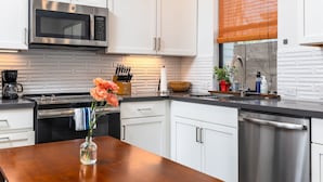 Una cucina moderna con mobili bianchi, un forno a microonde in acciaio inossidabile e un tavolo di legno con un vaso di fiori.