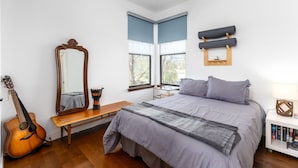 Una camera da letto con un letto, una chitarra, una panca, uno specchio e una finestra con persiane.