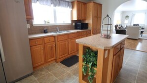 Una cucina con mobili in legno, un frigorifero in acciaio inox, un forno a microonde e una piccola isola con una pianta.
