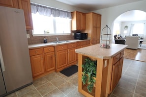 A kitchen with wooden cabinets, a stainless steel refrigerator, a microwave, and a small island with a plant. - Misty Meadows |Southern Lancaster Stay (Quarryville)