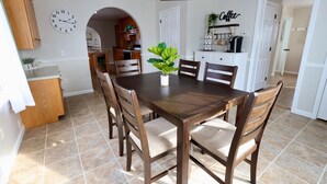 Zona pranzo con tavolo e sedie in legno, un orologio appeso al muro e un angolo caffè.
