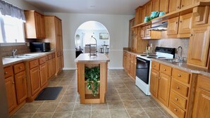 Una cucina con mobili in legno, un'isola centrale con piante, un forno a microonde, un fornello e un lavello.