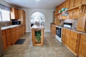 A kitchen with wooden cabinets, a central island with greenery, a microwave, stove, and sink. - Misty Meadows |Southern Lancaster Stay (Quarryville)