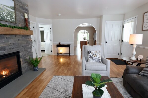 A living room with a fireplace, a grey sofa, a coffee table, and a lamp. - Misty Meadows |Southern Lancaster Stay (Quarryville)