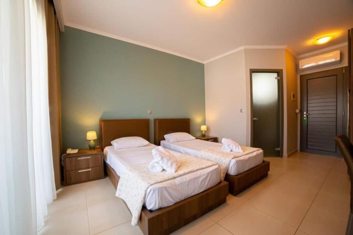 Une chambre d’hôtel avec deux lits simples, une table de chevet avec une lampe, une porte et une chaise.