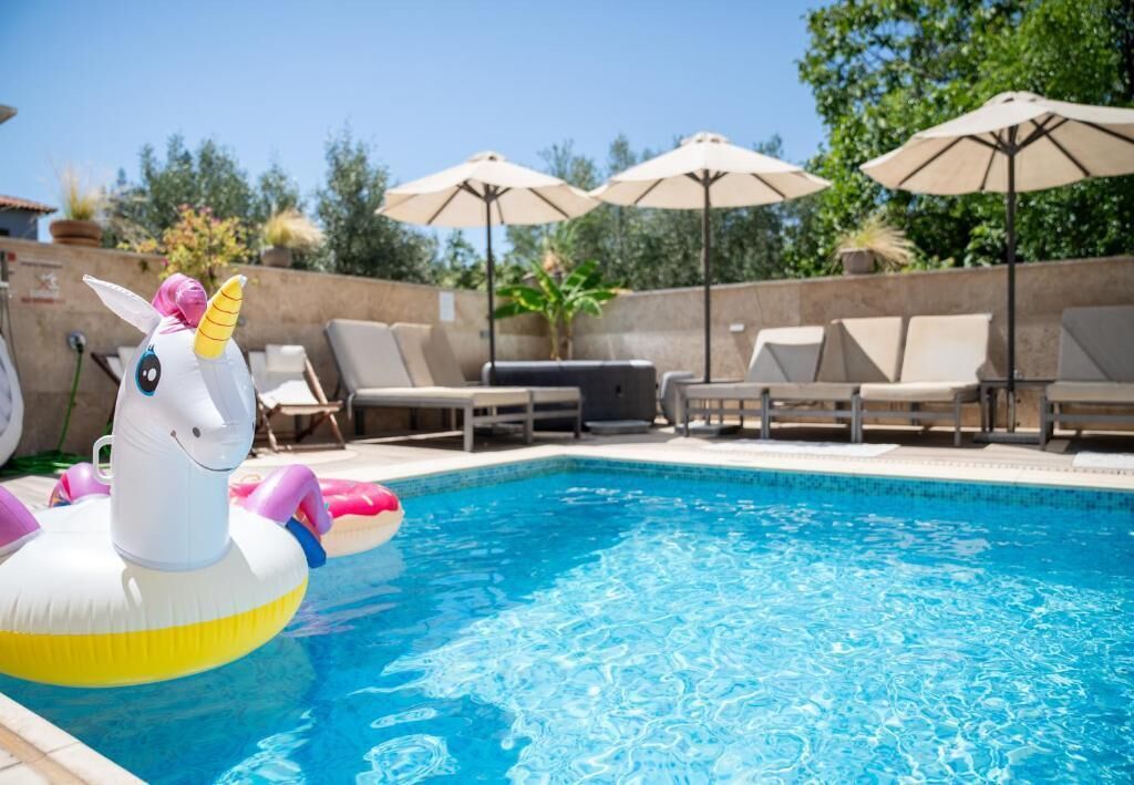 Una piscina con sillas de descanso y sombrillas, un flotador de unicornio y una parrilla.