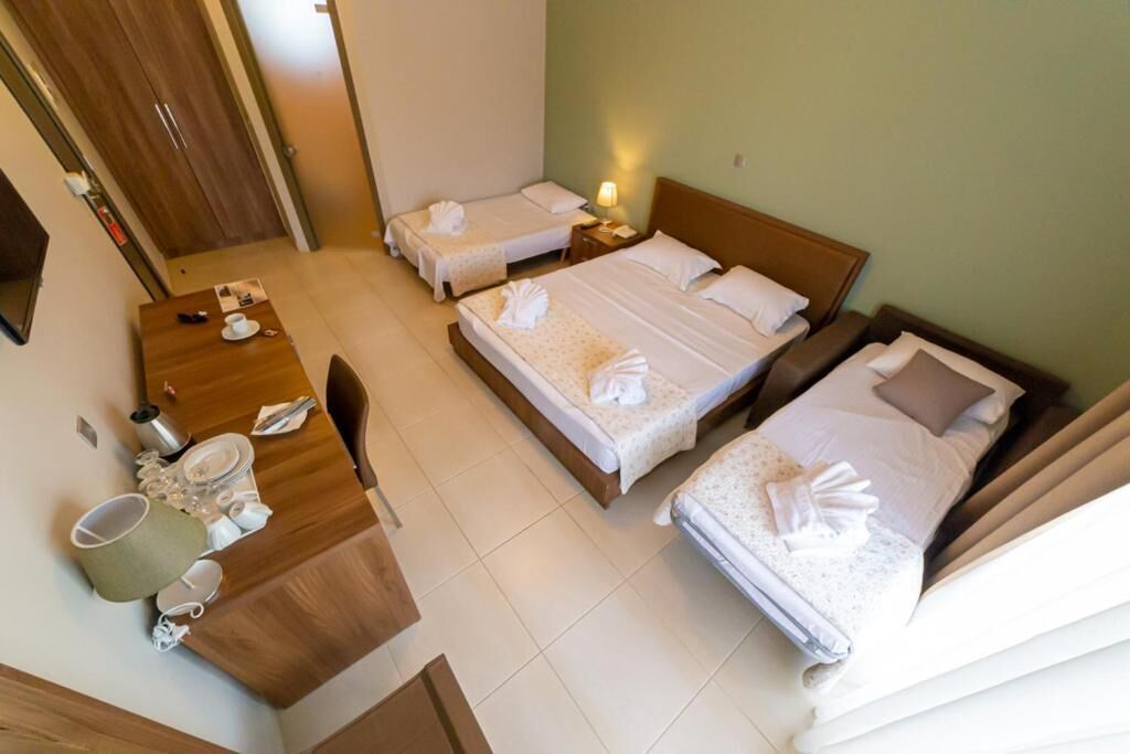 A hotel room with two beds, a wooden desk, a chair, and a small table with a lamp.