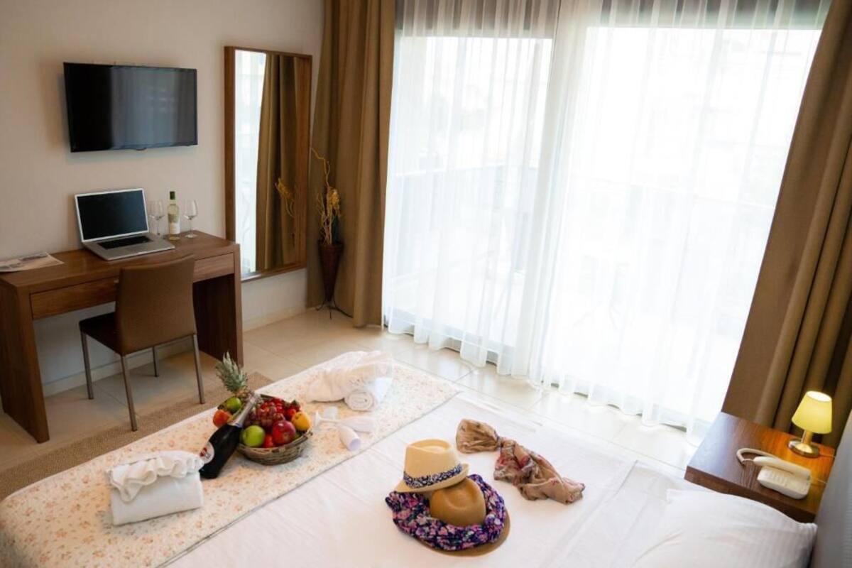 Une chambre d’hôtel avec un lit, un bureau avec un ordinateur portable, une télévision et une fenêtre avec des rideaux.