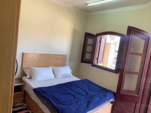 A single bed with a wooden headboard, white bedding, and a blue blanket.