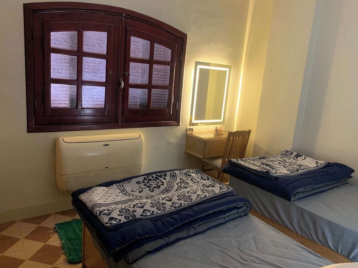 Quarto com duas camas, uma janela, um espelho, uma escrivaninha e um radiador.
