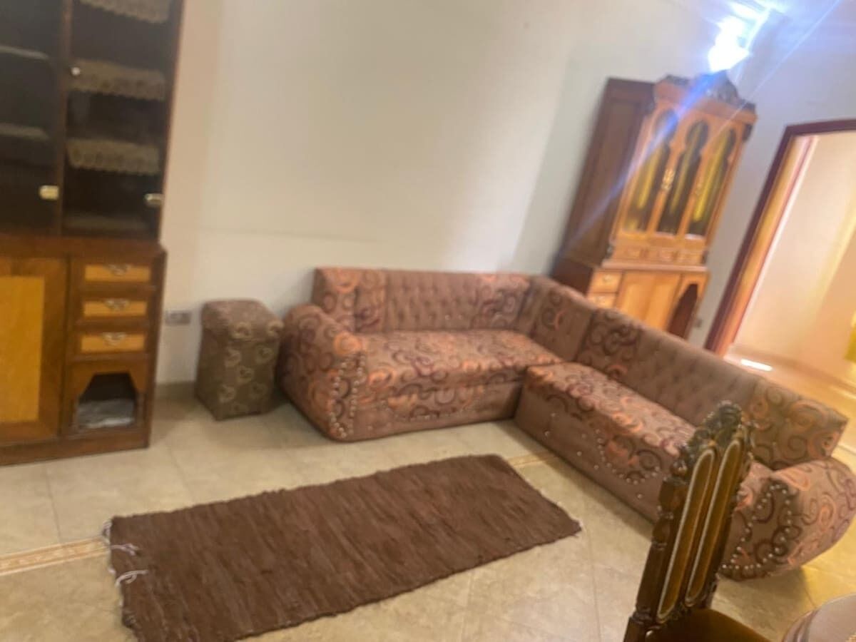 Ein Wohnzimmer mit einem gemusterten Sofa, einem braunen Teppich und einem Holzschrank.