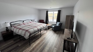 A bedroom with a bed, bedside table, lamp, chair, and a desk with a chair.