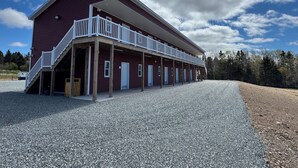 A red building with a covered porch and multiple doors, likely a motel or inn, with a gravel driveway and trees in the background.