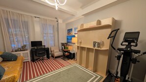 Ett kompakt bostadsutrymme med en säng, ett skrivbord, en stol, en motionscykel och en liten bokhylla.