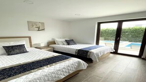 A hotel room with two beds, a small bedside table with a lamp, a painting on the wall, and a sliding glass door leading to a pool area. - Luxury 5 Bed, 7 Bath, Villa. Pool, Gym, Sauna, Hottub, Parking, 2 terr w/Seaview (Jursici)