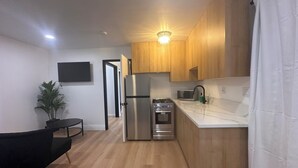 Une cuisine moderne avec des meubles en bois, un réfrigérateur en acier inoxydable, un four à micro-ondes et une cuisinière à gaz. On y trouve également une plante en pot et une chaise noire dans l’espace repas.