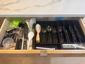 Eine Schublade mit verschiedenen Küchenutensilien, darunter Messer, Löffel und eine Reibe.