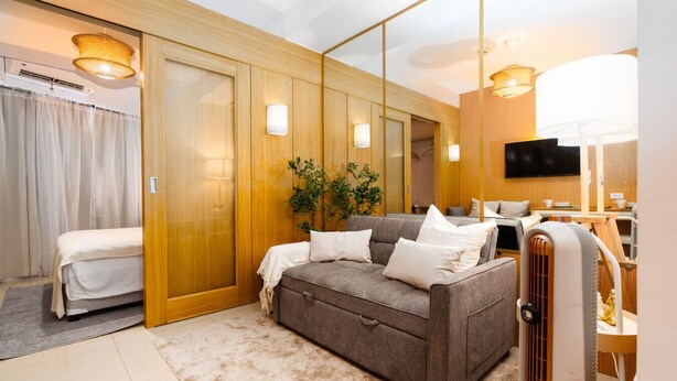 Una habitación de hotel moderna con sofá, una mesita, televisor y un espejo grande.