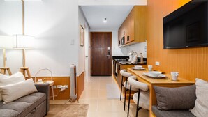 Un espacio habitable compacto con kitchenette, un sofá, una mesa de comedor y un televisor montado en la pared.