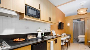 Una cocina compacta con microondas, pileta y taburetes de bar.