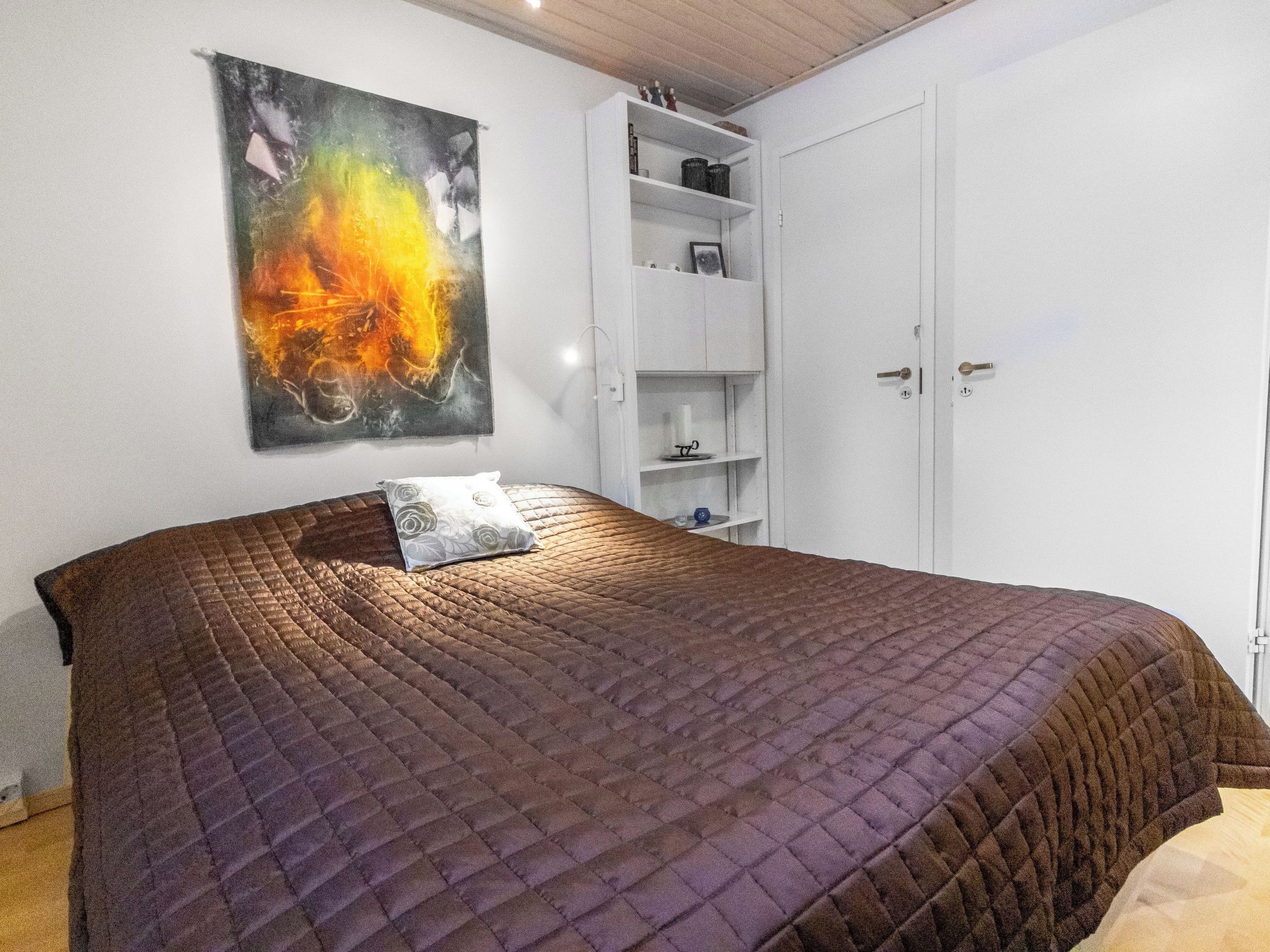 Une chambre à coucher avec un grand lit, une armoire blanche et une étagère contenant divers objets.