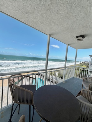 A covered outdoor area with a pool, chairs, and a view of the ocean. - Oceanfront & heated pool 2BR 2 BA condo large balcony, all new interior near ORL (Satellite Beach)