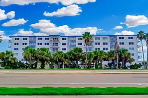 Een hotel met meerdere verdiepingen, een modern gevelontwerp, palmbomen ervoor en een helderblauwe lucht.
