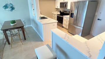 Eine moderne Küche mit weißen Schränken, einem Edelstahl-Kühlschrank und einer eingebauten Mikrowelle. Es gibt einen Essbereich mit Tisch und Stühlen.