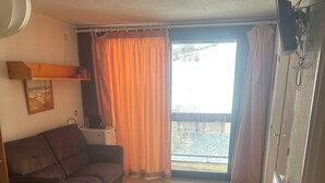 Ein kleines Wohnzimmer mit einer Couch, einem Tisch und einem Fenster mit Vorhängen.