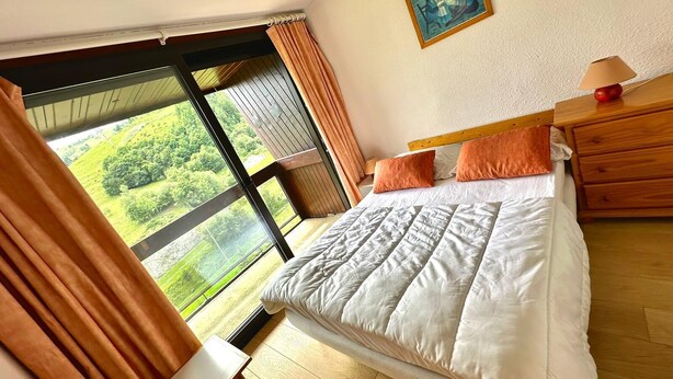 Ein Schlafzimmer mit großem Fenster, einem Bett, einem Nachttisch und einem Bild an der Wand.
