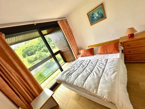 A bedroom with a large window, a bed, a nightstand, and a painting on the wall. - Corbier ski resort, summer and winter vacation rentals (Le Corbier)
