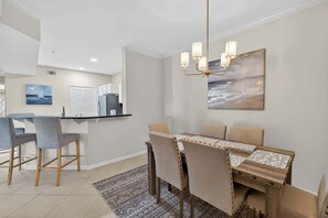 A dining area with a wooden table and chairs, a chandelier, and a painting on the wall. - Coastal Comfort 2 Queen Beds, pool, near beach! (St. Simons Island)