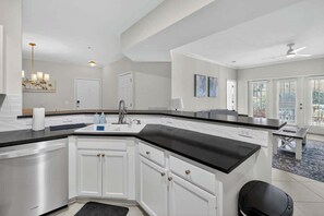 A modern kitchen with white cabinetry, a black countertop, and a built-in dishwasher. - Coastal Comfort 2 Queen Beds, pool, near beach! (St. Simons Island)