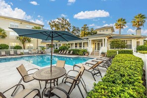 A poolside area with lounge chairs and a table, surrounded by well-maintained hedges and palm trees. - Coastal Comfort 2 Queen Beds, pool, near beach! (St. Simons Island)