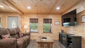 L’intérieur d’un chalet confortable, avec un canapé, une table basse, un téléviseur et une cheminée.