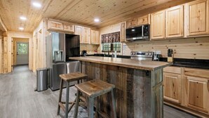 Une cuisine dotée de meubles en bois, d’un réfrigérateur en acier inoxydable, d’un four à micro-ondes et d’un grand îlot central avec des tabourets.