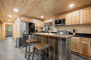 A kitchen with wooden cabinets, a stainless steel refrigerator, a microwave, and a large island with stools.