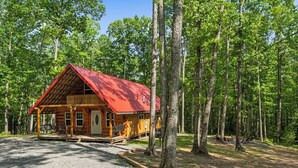 Une cabane avec un toit rouge, entourée d’arbres, et une allée gravillonnée.