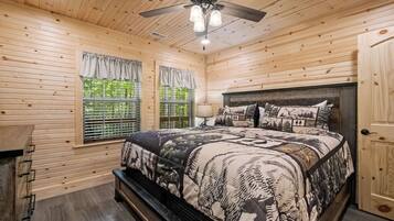 A wooden cabin bedroom with a bed, a ceiling fan, and a window with curtains.
