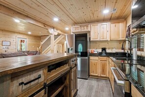A wooden cabin interior with a kitchen, wooden cabinets, a stainless steel refrigerator, and a wooden staircase.