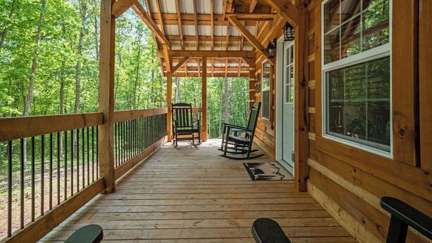 Une terrasse en bois dotée d’un espace abrité, de deux fauteuils à bascule et d’une porte donnant sur une pièce.