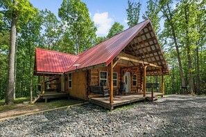 A cabin with a porch, wooden exterior, and a metal roof.