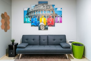 A living room with a sofa, a green trash bin, and a hexagonal wall decoration.