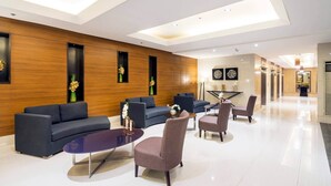 A modern lobby with dark sofas, a round coffee table, and a reception desk. - SkyLine CtyView Condotel BREEZE RESIDENCES near MOA,NAIA AIRPORT,PICC,US Embassy (Pasay City)