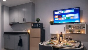 A modern kitchen with a flat-screen TV mounted above the counter, a built-in oven, and a dining area set for a meal with candles and wine glasses. - SkyLine CtyView Condotel BREEZE RESIDENCES near MOA,NAIA AIRPORT,PICC,US Embassy (Pasay City)