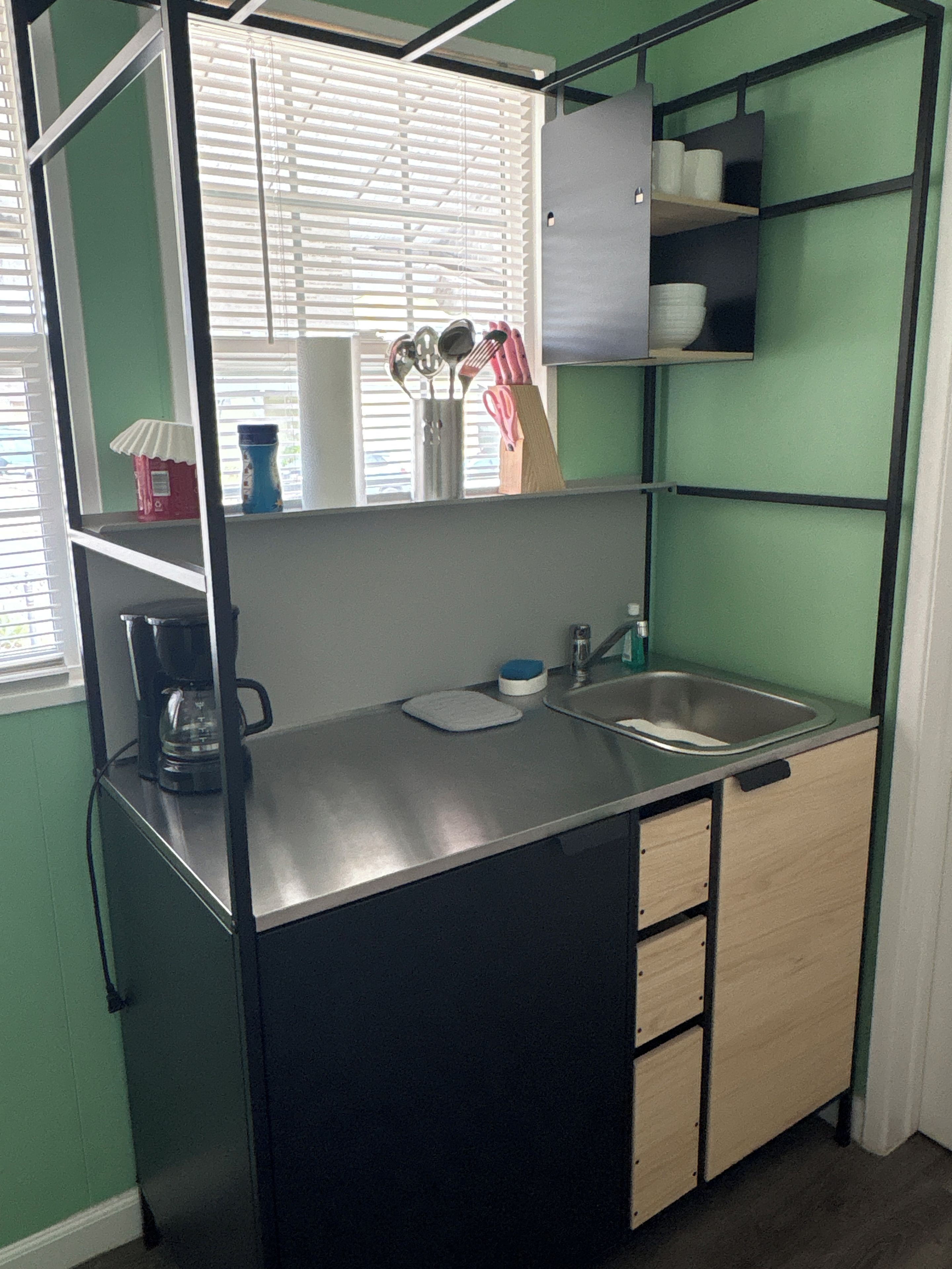 A compact kitchenette with a sink, a coffee maker, and a small countertop.