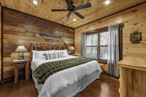 Ein Schlafzimmer einer Holzhütte mit Bett, Deckenventilator, Fenster mit Vorhängen und einer Holzwand mit einem Schild.
