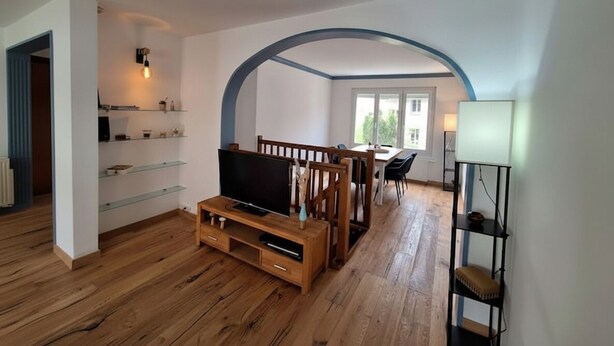 Una sala moderna con piso de madera, un mueble para televisión, un comedor con mesa y sillas, y un ventanal grande.